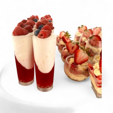 Two tall glasses with berry layers and mini desserts topped with strawberries and blueberries.