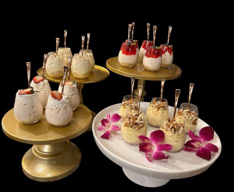 Assorted dessert cups with fruit, cream, and toppings on elegant stands with flower accents.