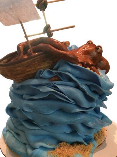 A whimsical cake featuring an octopus in a boat atop blue frosting waves.
