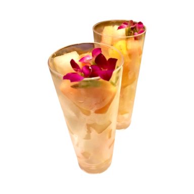 Two transparent glasses filled with tropical fruit and garnished with purple flowers.