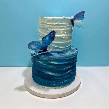 Two-tiered cake with blue and white waves, adorned with butterfly decorations.