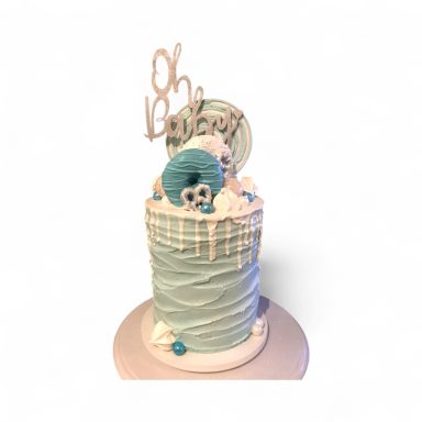 A two-tiered birthday cake with teal stripes, whipped cream, and a decorative "Oh Baby" topper.