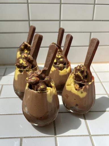 Five dessert cups filled with chocolate mousse and topped with yellow cream and chocolate pieces.