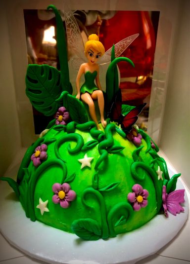 A green, fairy-themed cake with flowers, featuring a Tinkerbell figurine on top.
