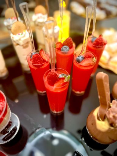 Colorful cocktails in small glasses with fruit garnishes on a reflective surface.