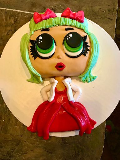 A cartoonish doll with big eyes, green hair, and a red dress on a round cake.