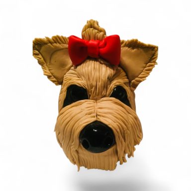 A cute dog head sculpture with textured fur and a red bow on its head.