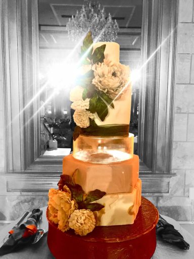 Three-tiered wedding cake decorated with flowers and leaves, with a glowing backdrop.