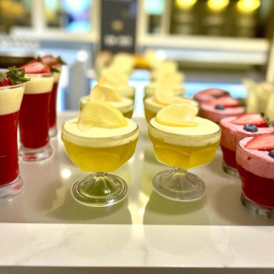 Colorful desserts in glass cups, featuring layers of fruit and creamy toppings.