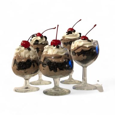 Five glasses of layered chocolate desserts topped with whipped cream and cherries.