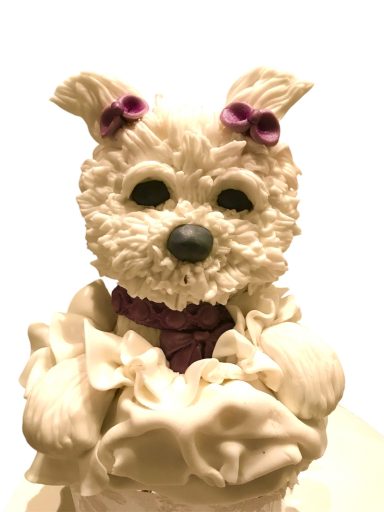 A cute, frosted dog cake with purple bows and a fluffy texture.